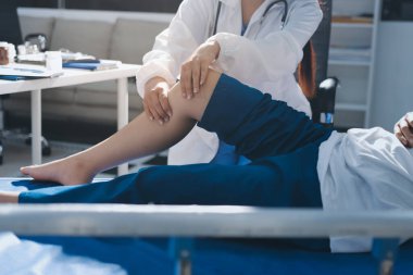 Kadın doktor elleri, erkek bir hastanın bacağını ve dizini uzatarak fizik tedavi uyguluyor.