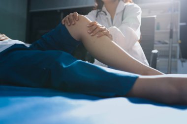 Kadın doktor elleri, erkek bir hastanın bacağını ve dizini uzatarak fizik tedavi uyguluyor.