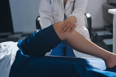 Kadın doktor elleri, erkek bir hastanın bacağını ve dizini uzatarak fizik tedavi uyguluyor.