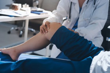 Kadın doktor elleri, erkek bir hastanın bacağını ve dizini uzatarak fizik tedavi uyguluyor.