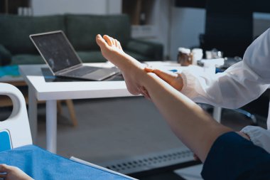Kadın doktor elleri, erkek bir hastanın bacağını ve dizini uzatarak fizik tedavi uyguluyor.