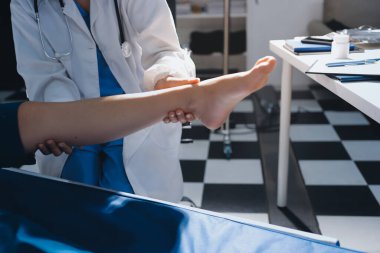 Kadın doktor elleri, erkek bir hastanın bacağını ve dizini uzatarak fizik tedavi uyguluyor.