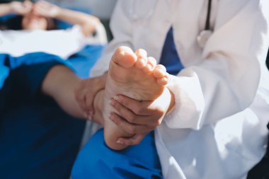 Kadın doktor elleri, erkek bir hastanın bacağını ve dizini uzatarak fizik tedavi uyguluyor.