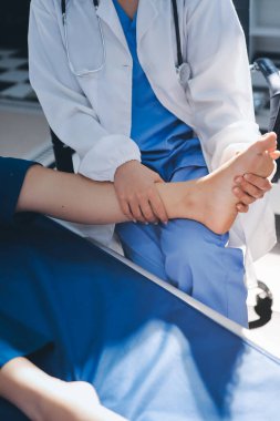 Kadın doktor elleri, erkek bir hastanın bacağını ve dizini uzatarak fizik tedavi uyguluyor.