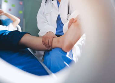 Kadın doktor elleri, erkek bir hastanın bacağını ve dizini uzatarak fizik tedavi uyguluyor.