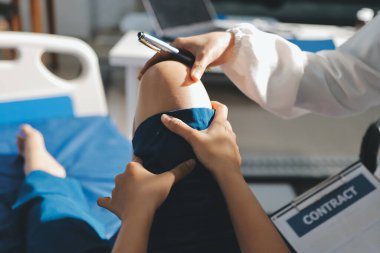 Kadın doktor elleri, erkek bir hastanın bacağını ve dizini uzatarak fizik tedavi uyguluyor.