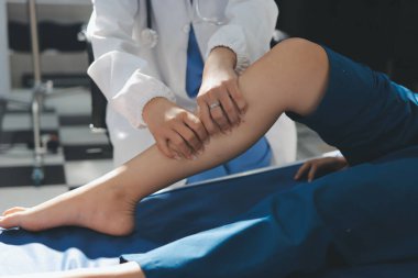 Kadın doktor elleri, erkek bir hastanın bacağını ve dizini uzatarak fizik tedavi uyguluyor.