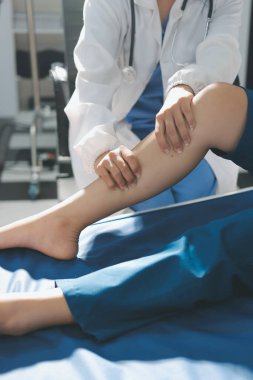 Kadın doktor elleri, erkek bir hastanın bacağını ve dizini uzatarak fizik tedavi uyguluyor.