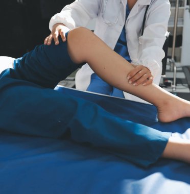 Kadın doktor elleri, erkek bir hastanın bacağını ve dizini uzatarak fizik tedavi uyguluyor.