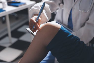 Kadın doktor elleri, erkek bir hastanın bacağını ve dizini uzatarak fizik tedavi uyguluyor.