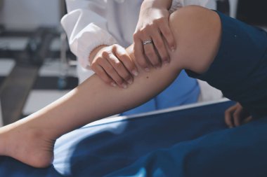Kadın doktor elleri, erkek bir hastanın bacağını ve dizini uzatarak fizik tedavi uyguluyor.