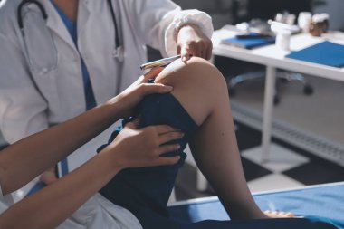 Kadın doktor elleri, erkek bir hastanın bacağını ve dizini uzatarak fizik tedavi uyguluyor.