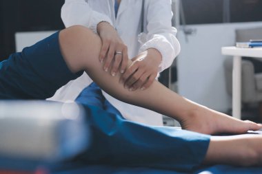 Kadın doktor elleri, erkek bir hastanın bacağını ve dizini uzatarak fizik tedavi uyguluyor.
