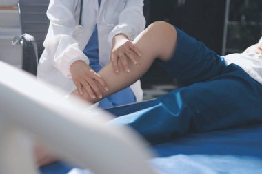 Kadın doktor elleri, erkek bir hastanın bacağını ve dizini uzatarak fizik tedavi uyguluyor.