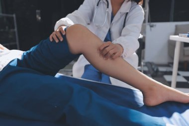 Kadın doktor elleri, erkek bir hastanın bacağını ve dizini uzatarak fizik tedavi uyguluyor.