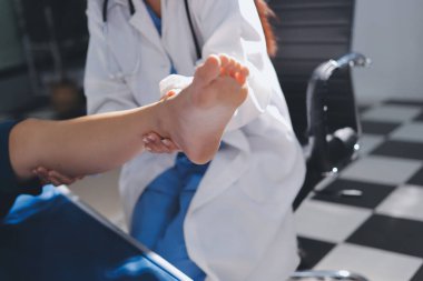 Kadın doktor elleri, erkek bir hastanın bacağını ve dizini uzatarak fizik tedavi uyguluyor.