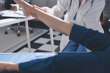 Kadın doktor elleri, erkek bir hastanın bacağını ve dizini uzatarak fizik tedavi uyguluyor.