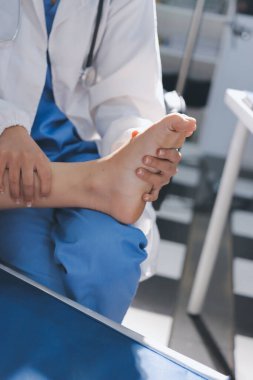 Kadın doktor elleri, erkek bir hastanın bacağını ve dizini uzatarak fizik tedavi uyguluyor.