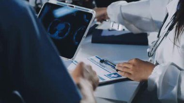 Hastane ofisinde dikilirken elinde dijital tablet olan beyaz üniformalı genç bir erkek doktor.