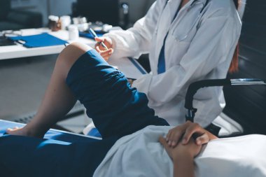 Kadın doktor elleri, erkek bir hastanın bacağını ve dizini uzatarak fizik tedavi uyguluyor.