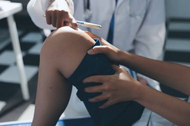 Kadın doktor elleri, erkek bir hastanın bacağını ve dizini uzatarak fizik tedavi uyguluyor.