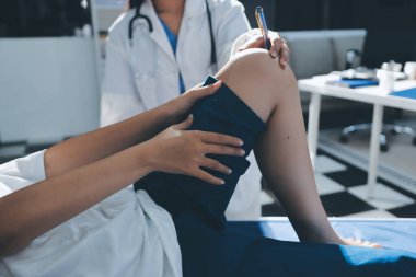 Kadın doktor elleri, erkek bir hastanın bacağını ve dizini uzatarak fizik tedavi uyguluyor.