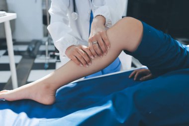 Kadın doktor elleri, erkek bir hastanın bacağını ve dizini uzatarak fizik tedavi uyguluyor.