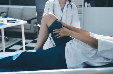 Kadın doktor elleri, erkek bir hastanın bacağını ve dizini uzatarak fizik tedavi uyguluyor.