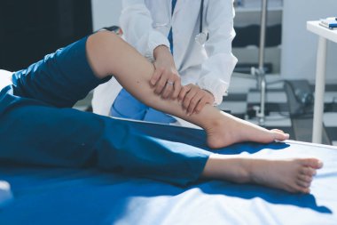 Kadın doktor elleri, erkek bir hastanın bacağını ve dizini uzatarak fizik tedavi uyguluyor.
