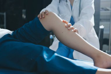 Kadın doktor elleri, erkek bir hastanın bacağını ve dizini uzatarak fizik tedavi uyguluyor.