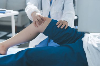 Kadın doktor elleri, erkek bir hastanın bacağını ve dizini uzatarak fizik tedavi uyguluyor.