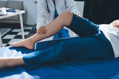 Kadın doktor elleri, erkek bir hastanın bacağını ve dizini uzatarak fizik tedavi uyguluyor.
