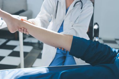 Kadın doktor elleri, erkek bir hastanın bacağını ve dizini uzatarak fizik tedavi uyguluyor.