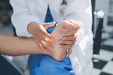 Kadın doktor elleri, erkek bir hastanın bacağını ve dizini uzatarak fizik tedavi uyguluyor.