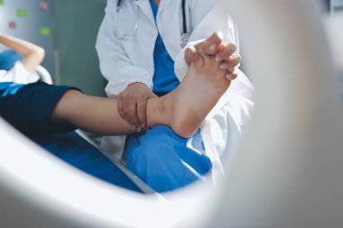 Kadın doktor elleri, erkek bir hastanın bacağını ve dizini uzatarak fizik tedavi uyguluyor.