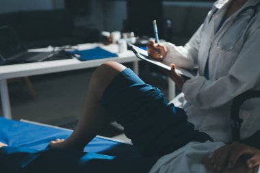 Kadın doktor elleri, erkek bir hastanın bacağını ve dizini uzatarak fizik tedavi uyguluyor.