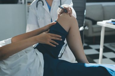 Kadın doktor elleri, erkek bir hastanın bacağını ve dizini uzatarak fizik tedavi uyguluyor.