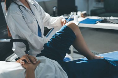 Kadın doktor elleri, erkek bir hastanın bacağını ve dizini uzatarak fizik tedavi uyguluyor.