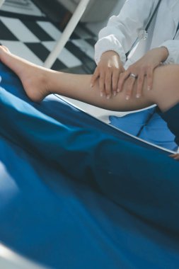 Kadın doktor elleri, erkek bir hastanın bacağını ve dizini uzatarak fizik tedavi uyguluyor.