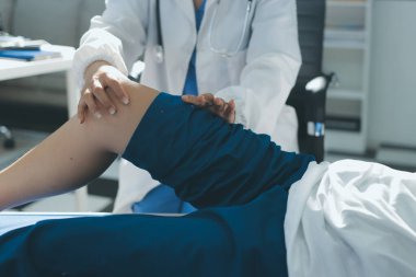 Kadın doktor elleri, erkek bir hastanın bacağını ve dizini uzatarak fizik tedavi uyguluyor.