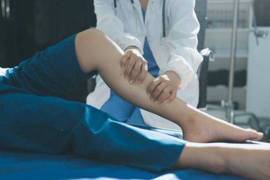Kadın doktor elleri, erkek bir hastanın bacağını ve dizini uzatarak fizik tedavi uyguluyor.