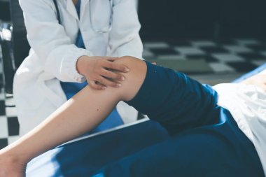 Kadın doktor elleri, erkek bir hastanın bacağını ve dizini uzatarak fizik tedavi uyguluyor.