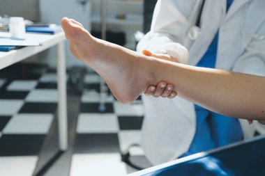 Kadın doktor elleri, erkek bir hastanın bacağını ve dizini uzatarak fizik tedavi uyguluyor.