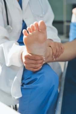 Kadın doktor elleri, erkek bir hastanın bacağını ve dizini uzatarak fizik tedavi uyguluyor.