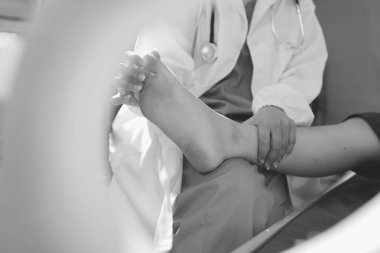 Kadın doktor elleri, erkek bir hastanın bacağını ve dizini uzatarak fizik tedavi uyguluyor.