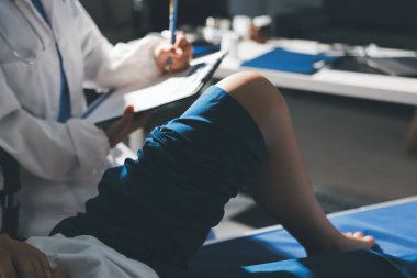 Kadın doktor elleri, erkek bir hastanın bacağını ve dizini uzatarak fizik tedavi uyguluyor.