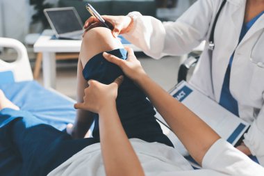 Kadın doktor elleri, erkek bir hastanın bacağını ve dizini uzatarak fizik tedavi uyguluyor.