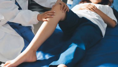 Kadın doktor elleri, erkek bir hastanın bacağını ve dizini uzatarak fizik tedavi uyguluyor.