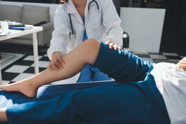 Kadın doktor elleri, erkek bir hastanın bacağını ve dizini uzatarak fizik tedavi uyguluyor.