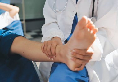 Kadın doktor elleri, erkek bir hastanın bacağını ve dizini uzatarak fizik tedavi uyguluyor.